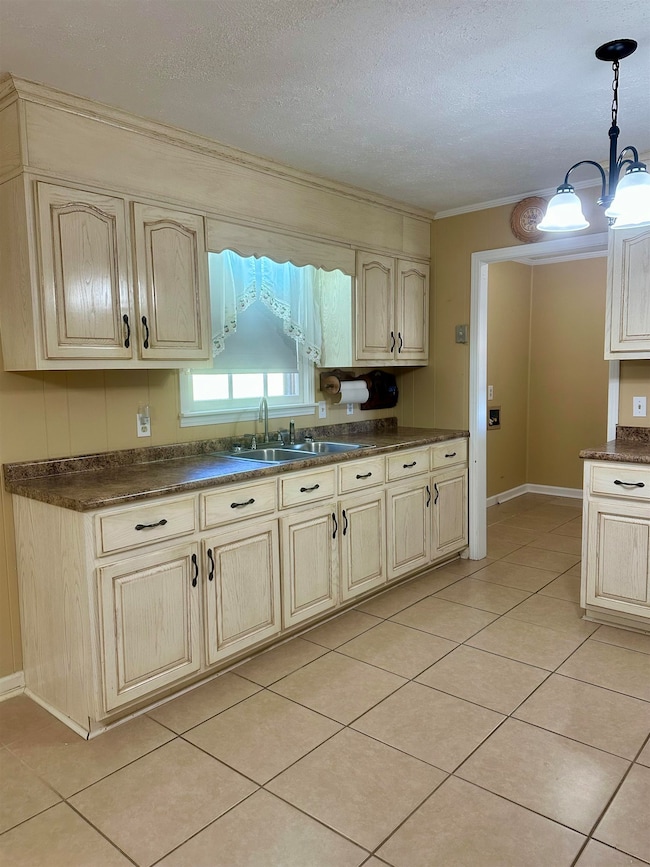 Kitchen featuring dark countertops, light tile patterned floors, pendant lighting, a textured ceiling, and cream cabinets