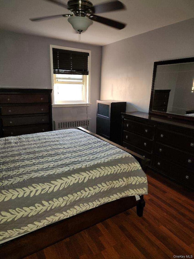 Bedroom with a ceiling fan, dark wood finished floors, and radiator heating unit