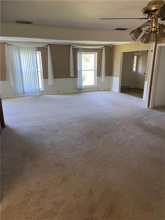 Carpeted spare room with a textured ceiling, a ceiling fan, and wainscoting