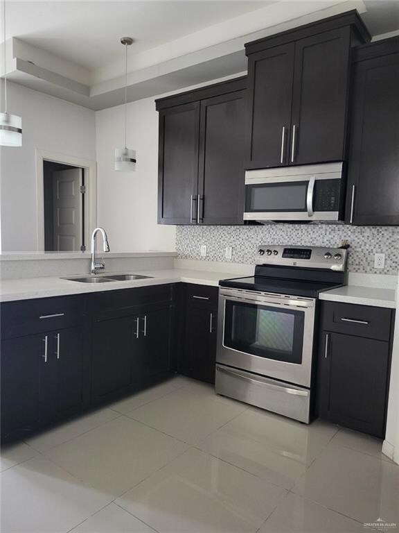 Kitchen featuring stainless steel appliances, dark cabinets, light tile patterned flooring, light countertops, and decorative light fixtures