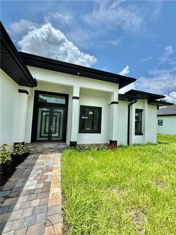 Property entrance with stucco siding, french doors, and a yard