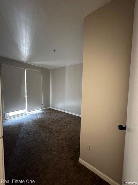 Empty room with dark colored carpet and baseboards