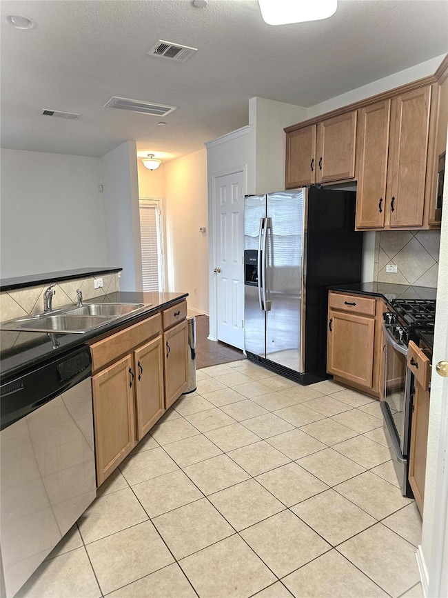 Kitchen featuring decorative backsplash, stainless steel appliances, light tile patterned floors, brown cabinets, and a textured ceiling