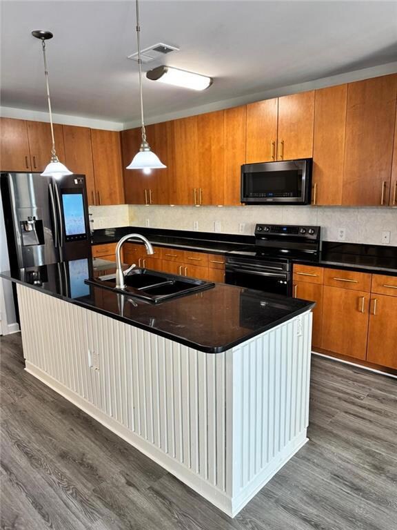 Kitchen with sink, dark wood-type flooring, stainless steel appliances, decorative light fixtures, and a center island with sink