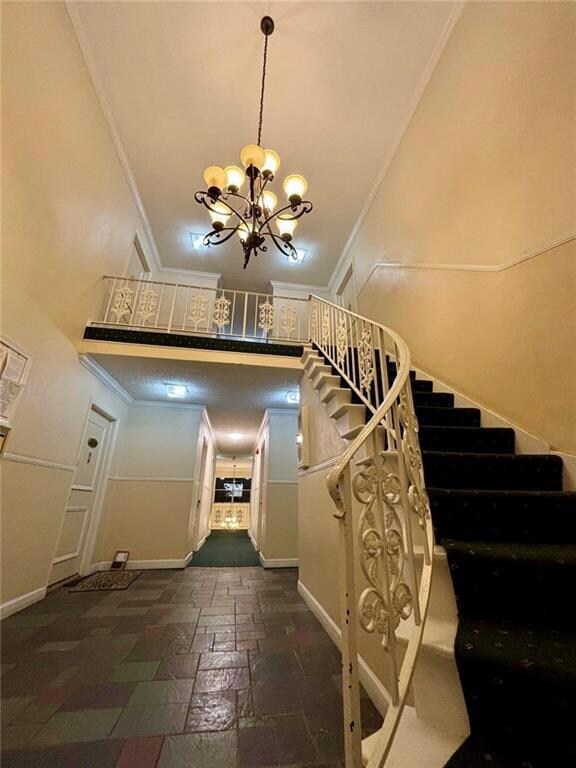 Stairs with crown molding, a chandelier, baseboards, a high ceiling, and stone tile flooring