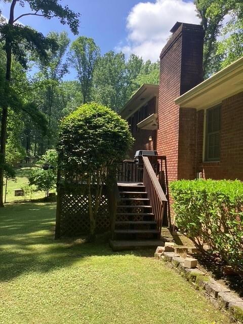 View of grassy yard featuring a wooden deck and stairs