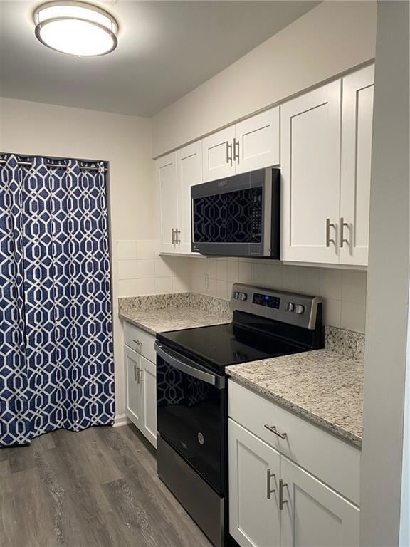 Kitchen with black range oven, white cabinetry, stainless steel microwave, and dark wood-type flooring