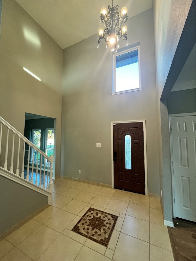 Tiled entryway with a high ceiling, healthy amount of natural light, a chandelier, and stairs