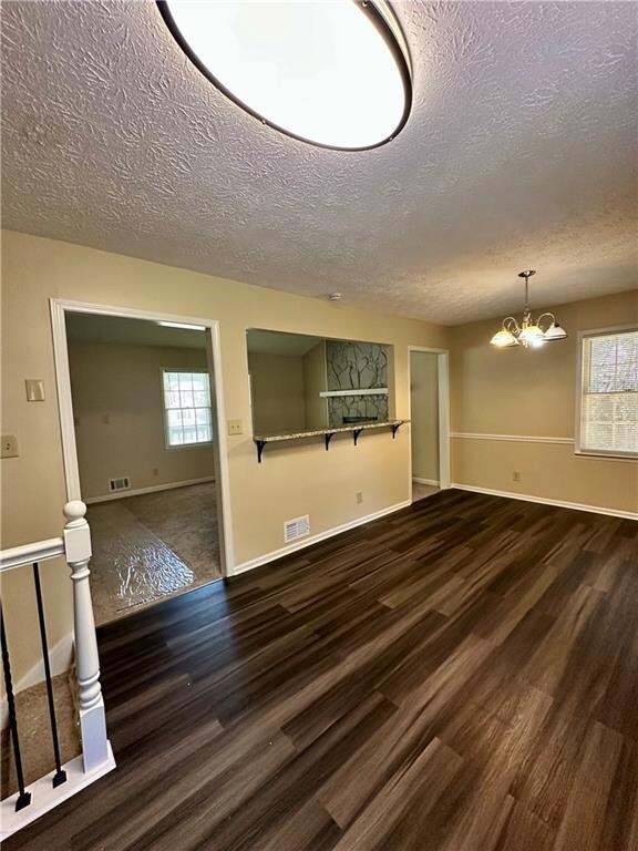 Unfurnished living room with a textured ceiling, dark wood-style flooring, and a chandelier