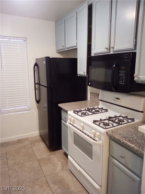 Kitchen with gas range gas stove, black microwave, gray cabinets, and light tile patterned floors
