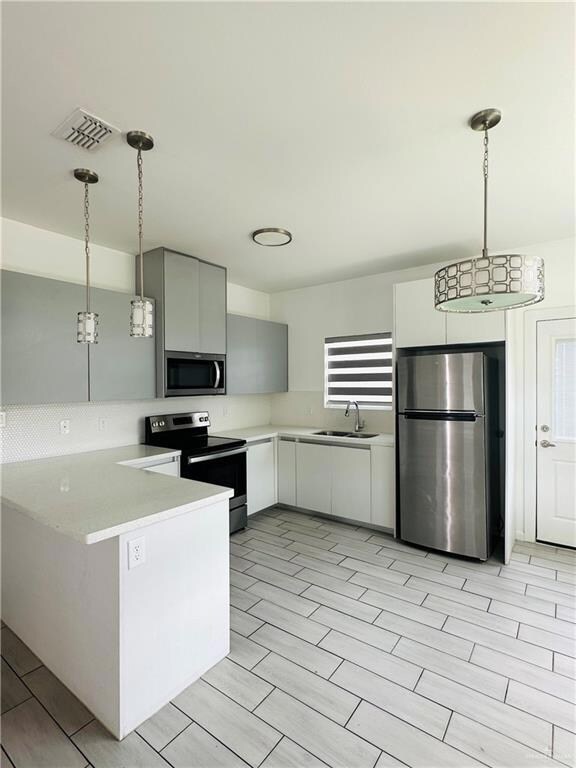 Kitchen with light countertops, visible vents, stainless steel appliances, and a sink