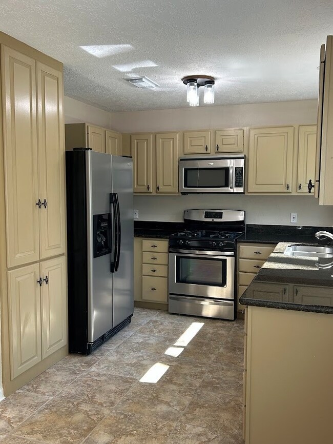 This kitchen features stainless steel appliances, including a fridge and stove and cabinetry. It also has a tile floor and ample storage space.  The window above the sink really lights up the space.