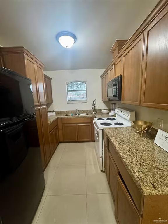 Kitchen with black appliances, light stone counters, light tile patterned floors, brown cabinets, and a sink