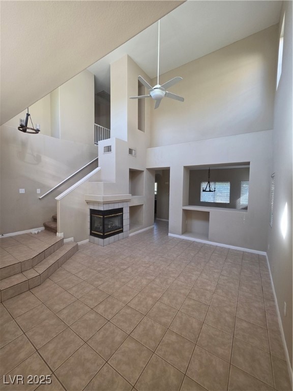 Unfurnished living room featuring built in features, light tile patterned flooring, high vaulted ceiling, a tile fireplace, and a ceiling fan