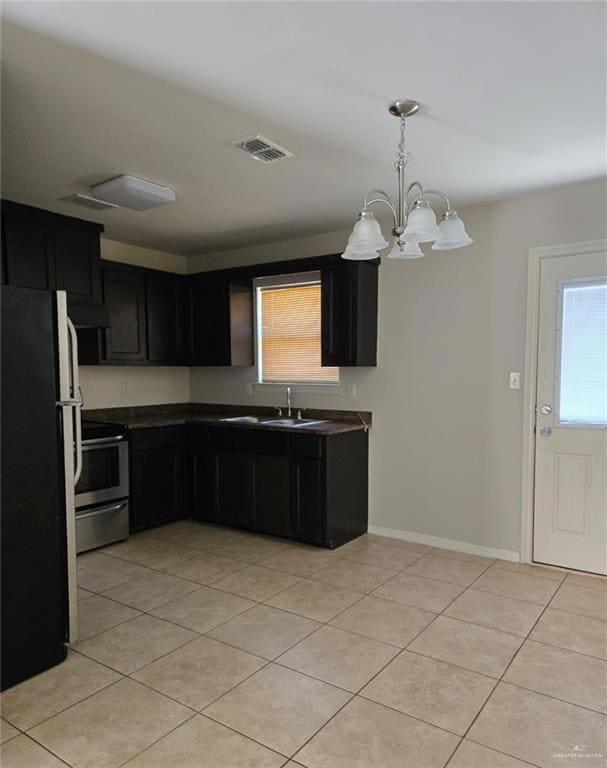 Kitchen featuring dark countertops, freestanding refrigerator, dark cabinetry, hanging light fixtures, and stainless steel electric range
