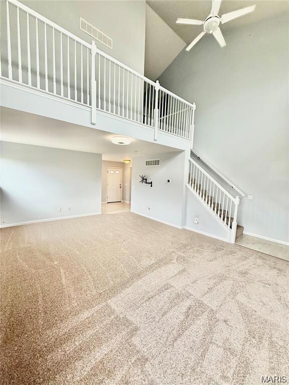 Unfurnished living room featuring high vaulted ceiling, light colored carpet, ceiling fan, and stairway