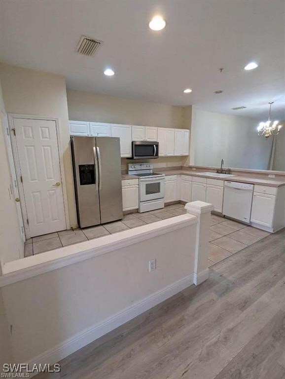 Kitchen with light wood-type flooring, a chandelier, sink, appliances with stainless steel finishes, and white cabinets
