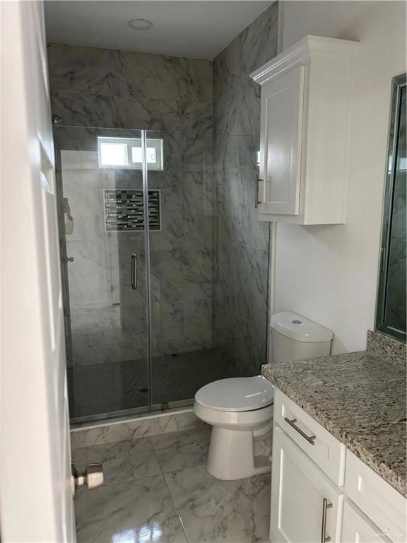 Bathroom featuring toilet, tile flooring, a shower with shower door, and vanity