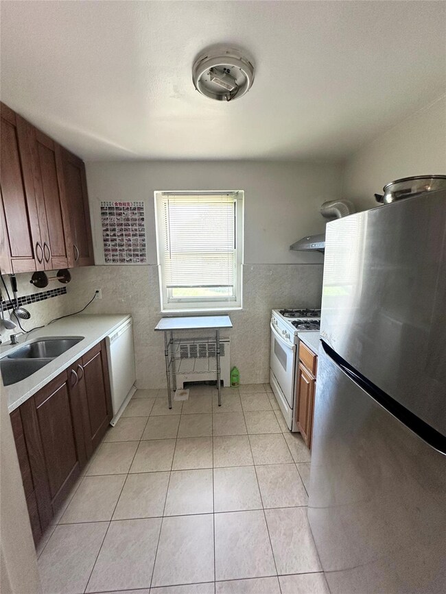 Kitchen featuring white appliances, radiator, light countertops, tile walls, and wall chimney range hood