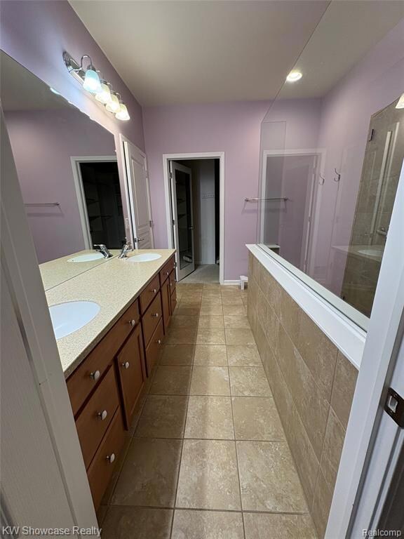 Bathroom featuring a walk in closet, double vanity, a tile shower, light tile patterned floors, and recessed lighting