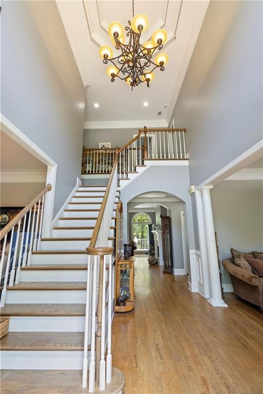 Stairs with arched walkways, a high ceiling, a chandelier, ornamental molding, and hardwood floors