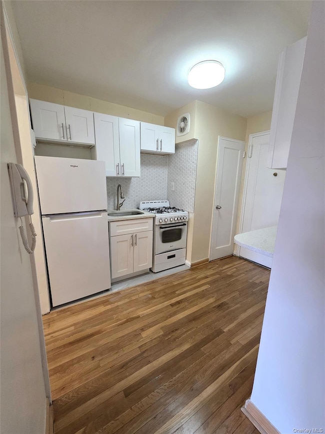 Kitchen featuring white appliances, white cabinetry, tasteful backsplash, light wood finished floors, and light countertops