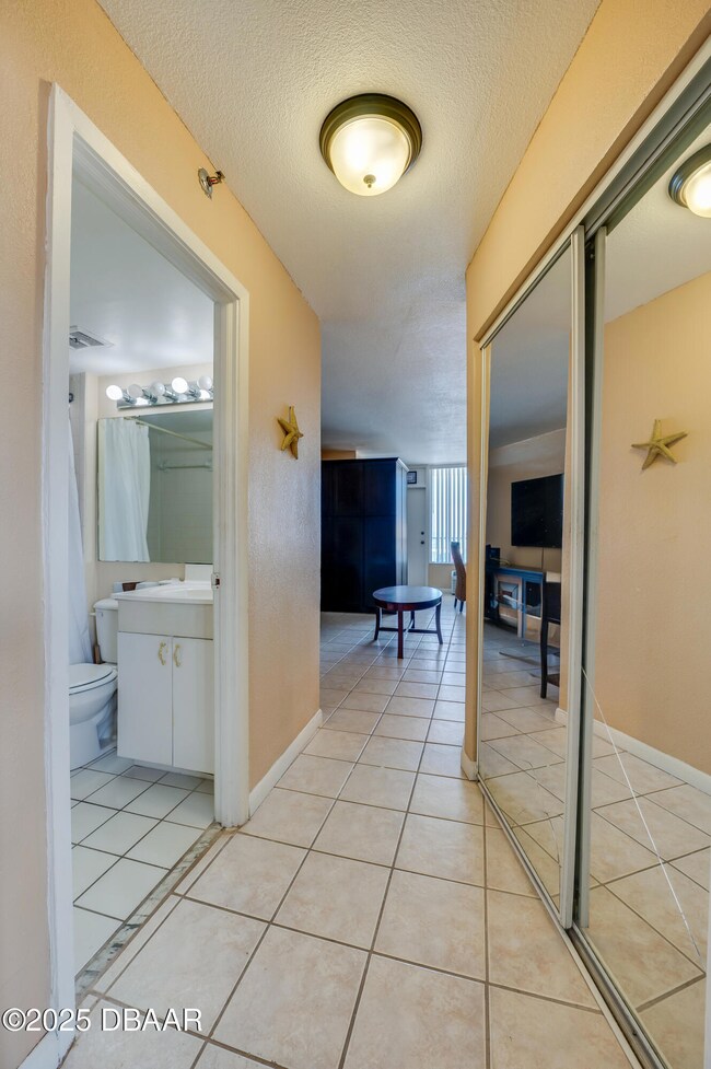 Entrance with tile flooring and mirrored closet doors leads to both the bathroom and living area.