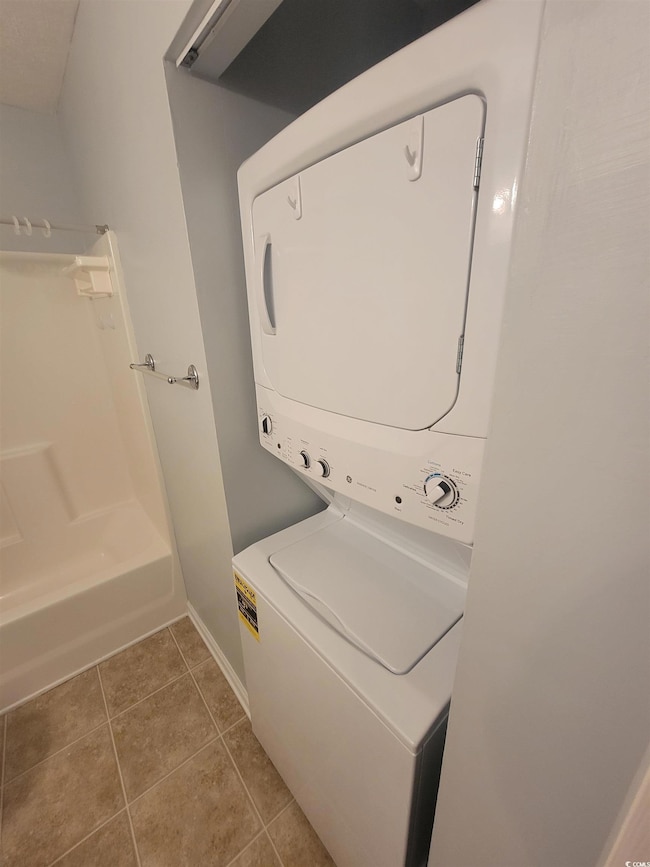 Laundry area featuring estacked washer and dryer, tile patterned flooring, and baseboards