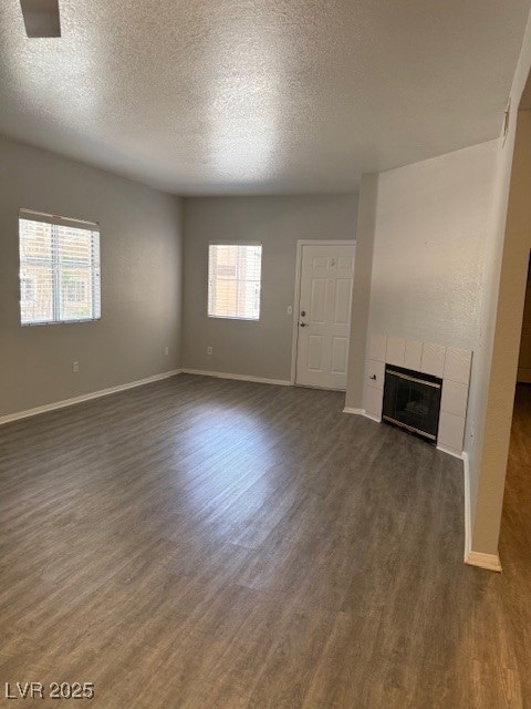 Unfurnished living room featuring a textured ceiling, dark wood-type flooring, and a tiled fireplace