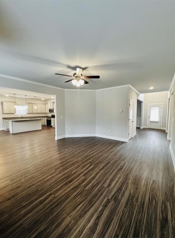 Unfurnished living room with ceiling fan, dark wood-style floors, baseboards, and ornamental molding