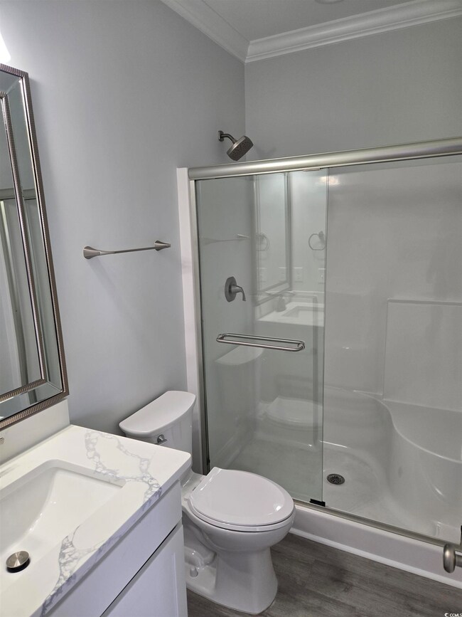 Full bathroom featuring toilet, wood finished floors, vanity, a stall shower, and crown molding