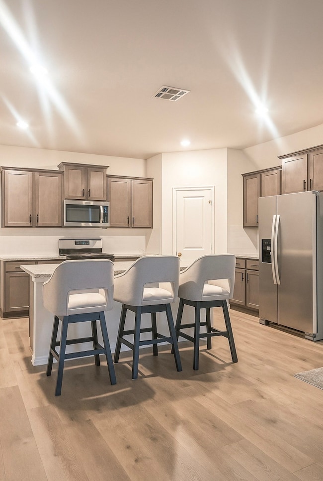 Kitchen featuring a kitchen bar, a kitchen island with sink, appliances with stainless steel finishes, light wood finished floors, and recessed lighting