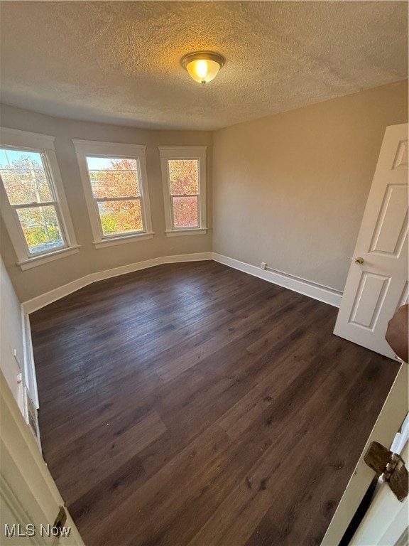 Empty room featuring a textured ceiling and dark wood-style flooring