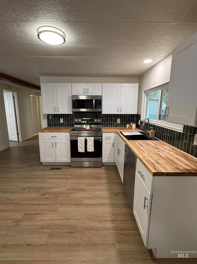 Kitchen featuring wood counters, decorative backsplash, white cabinetry, appliances with stainless steel finishes, and a textured ceiling