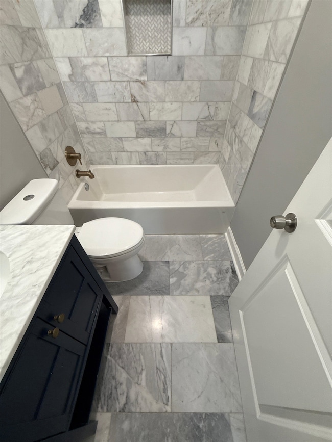 Full bath featuring vanity, marble finish flooring, and washtub / shower combination