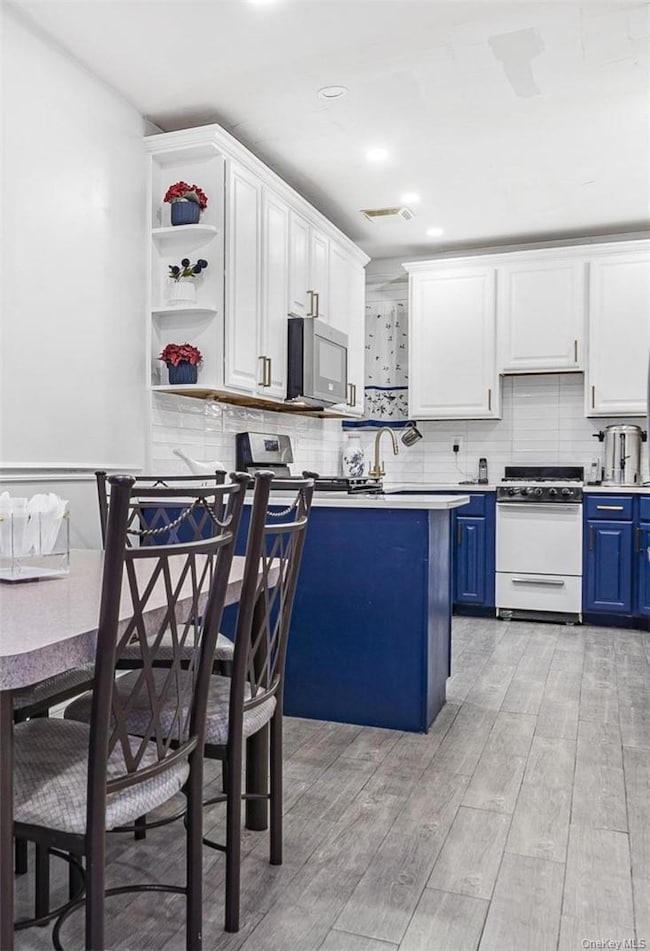 Kitchen featuring light wood-type flooring, blue cabinetry, white cabinetry, backsplash, and appliances with stainless steel finishes
