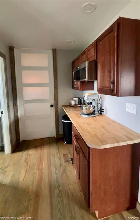 Kitchen featuring light wood finished floors, stainless steel microwave, brown cabinets, and butcher block counters