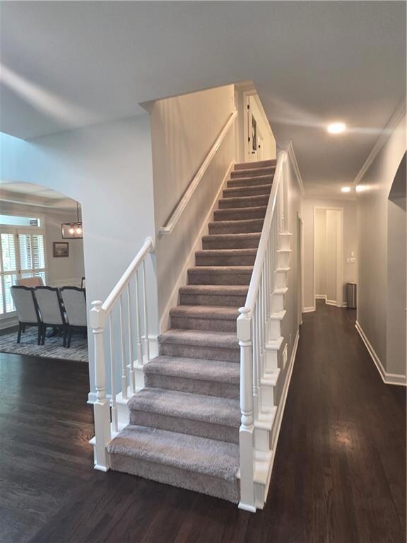 Stairs featuring arched walkways, wood finished floors, and ornamental molding