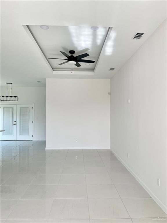 Spare room with a tray ceiling, light tile floors, and ceiling fan
