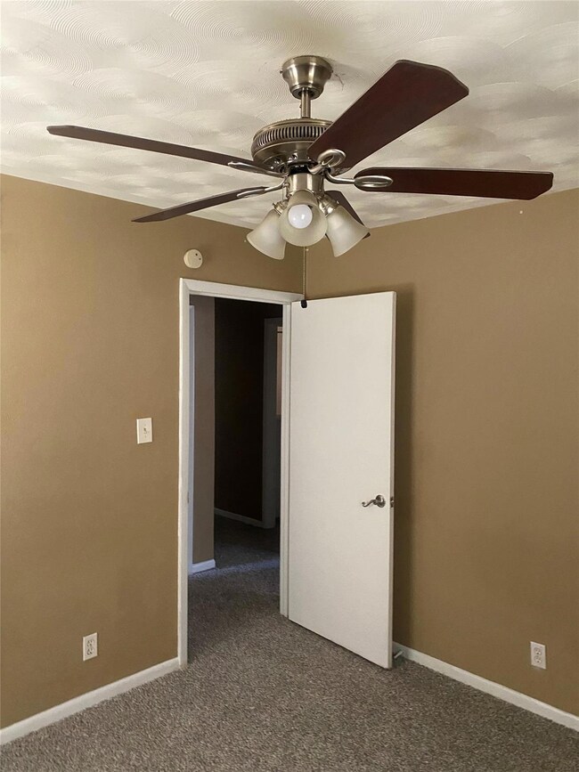 Carpeted spare room featuring ceiling fan and base