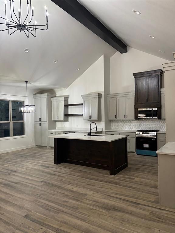 Kitchen featuring stainless steel appliances, a chandelier, light countertops, open shelves, and an island with sink