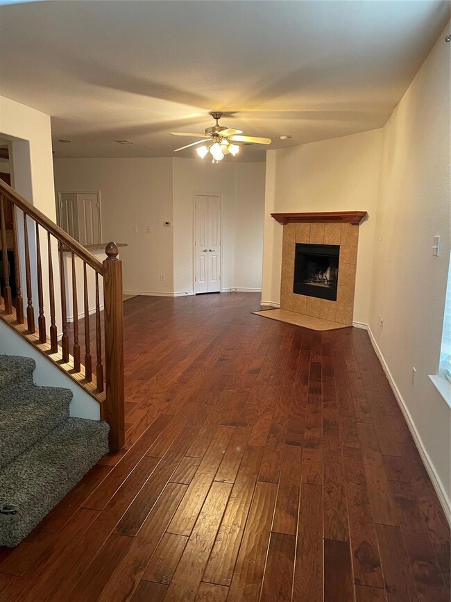 Unfurnished living room featuring dark hardwood / wood-style floors, a tile fireplace, and ceiling fan