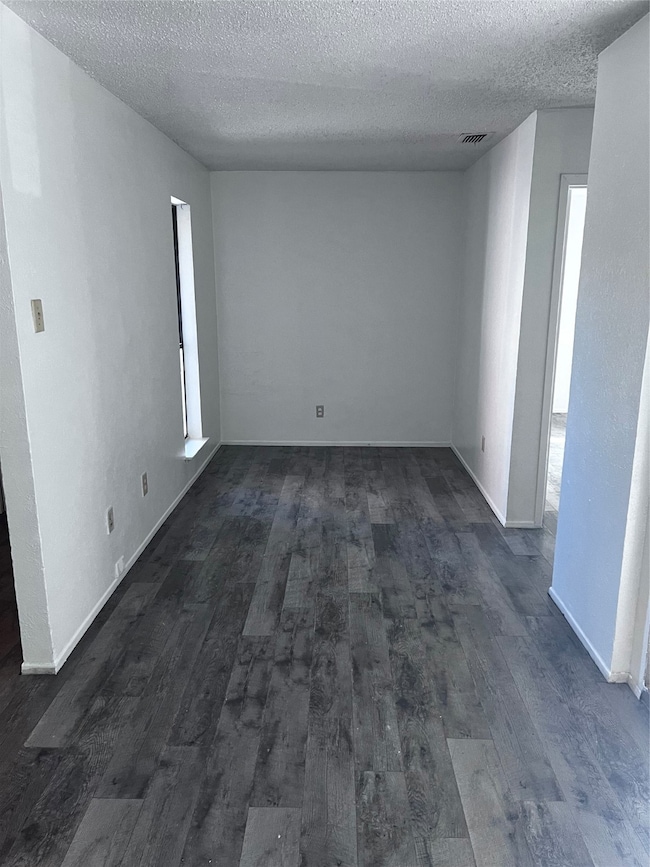 Empty room with a textured ceiling and dark wood-type flooring
