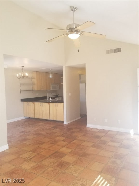 Unfurnished living room featuring ceiling fan, high vaulted ceiling, and a chandelier
