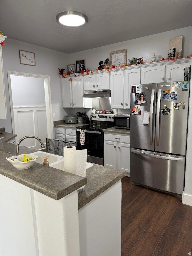 Kitchen with stainless steel appliances, dark wood-style flooring, white cabinetry, dark countertops, and a peninsula