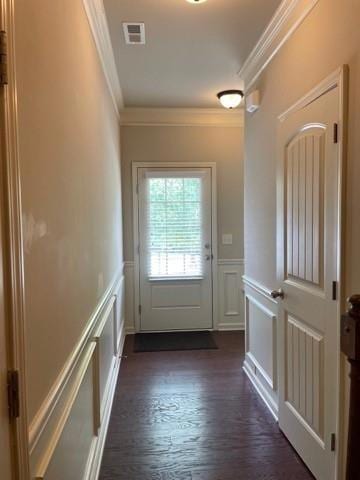 Doorway to outside with ornamental molding, a decorative wall, dark wood-style floors, and wainscoting
