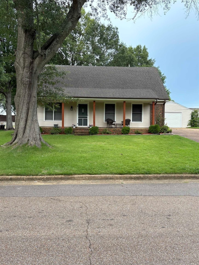 View of front of house with a porch, a front yard, brick siding, roof with shingles, and a detached garage