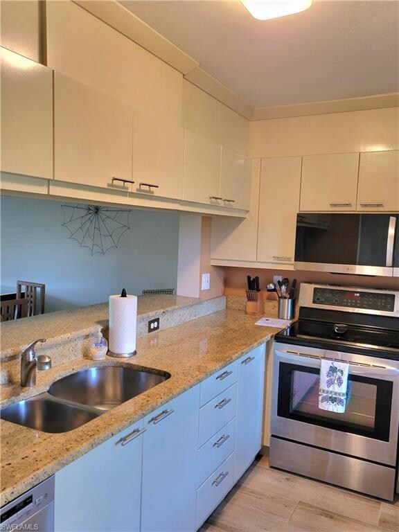 Kitchen with stainless steel appliances, light stone countertops, light wood finished floors, and white cabinetry