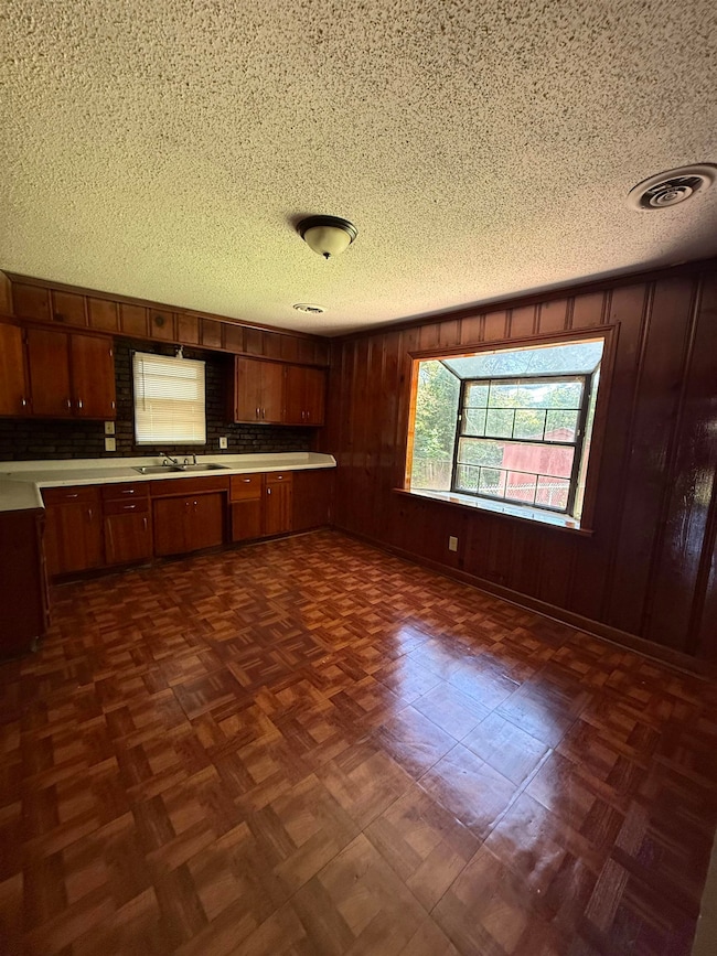Kitchen featuring a sink, light countertops, a textured ceiling, backsplash, and brown cabinetry