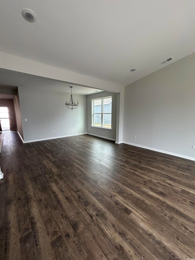 Spare room with a notable chandelier, dark wood-ty